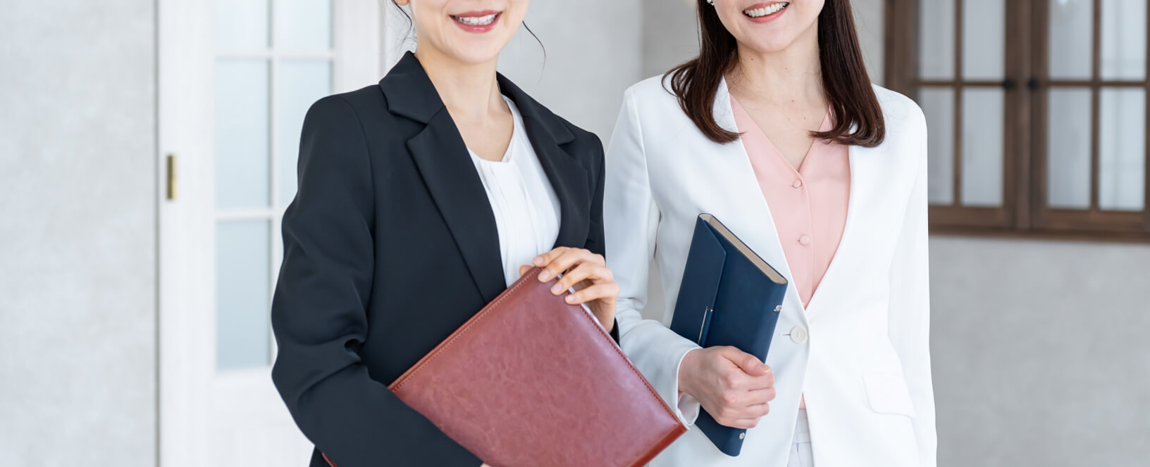 スーツ姿の女性2人が書類を手に持ち笑顔で立っている様子