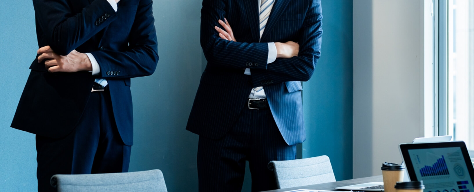 スーツ姿の男性2人が会議室で腕を組んで打ち合わせしている様子